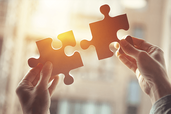 Puzzle pieces being held together by two hands in the sunlight.