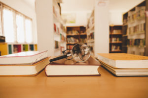 Book in library with old open textbook, stack piles of literature text archive on reading desk, and aisle of bookshelves in school study class room background for academic education learning concept