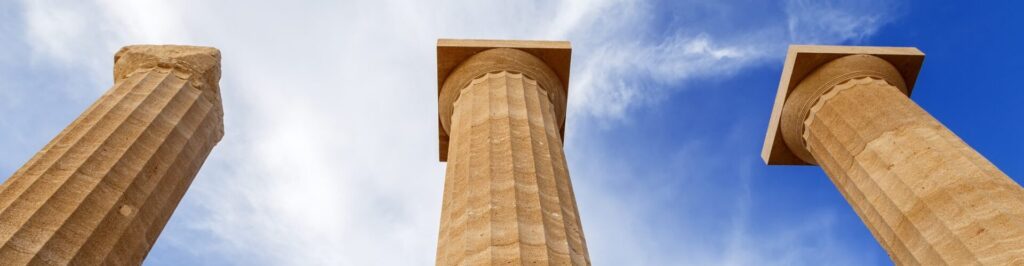 Three ancient greek pillars against a blue sky.