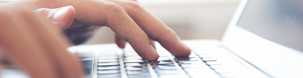 Close-up of male hands typing on laptop keyboard indoors. Businessman working in office or student browsing information