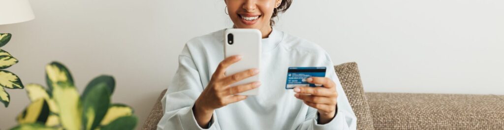 Smiling woman using smartphone and credit card. Young female making a purchase online.