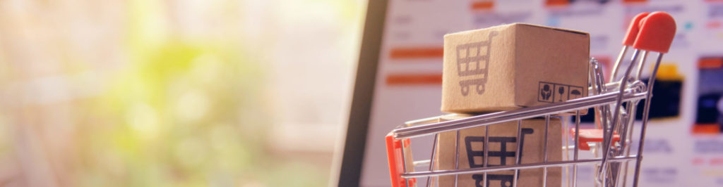 Parcel or Paper cartons with a shopping cart logo in a trolley on a laptop keyboard.