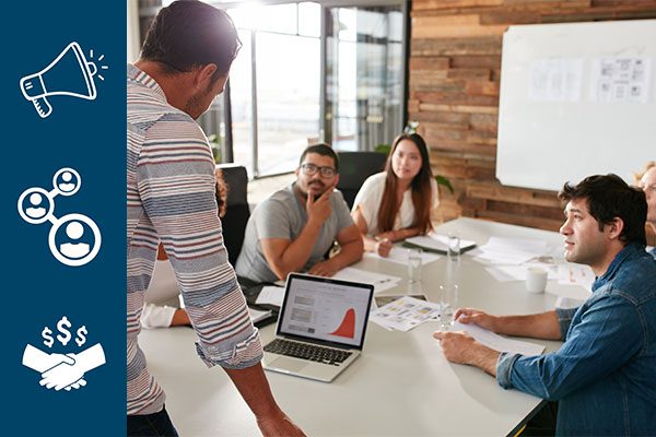 People sitting at a table at an agency with a navy bar of marketing icons on the left.