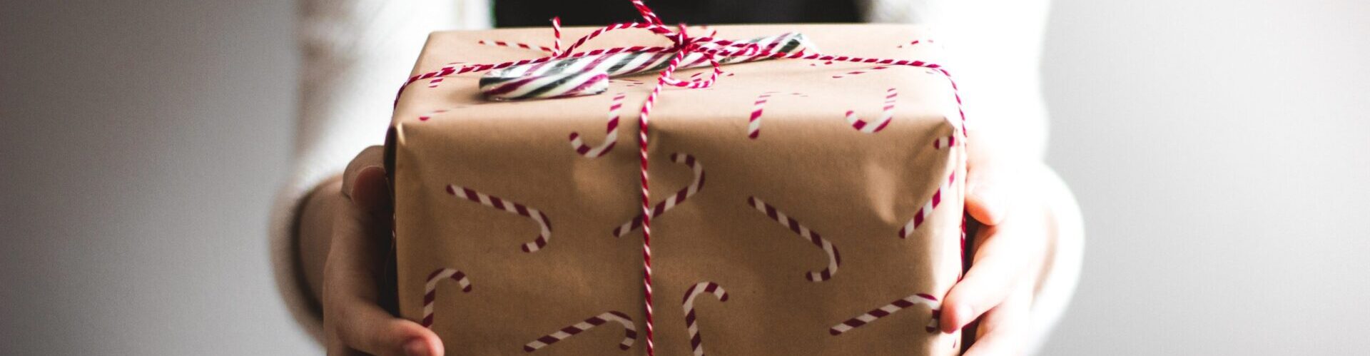 Woman holding present wrapped in candy cane wrapping paper.
