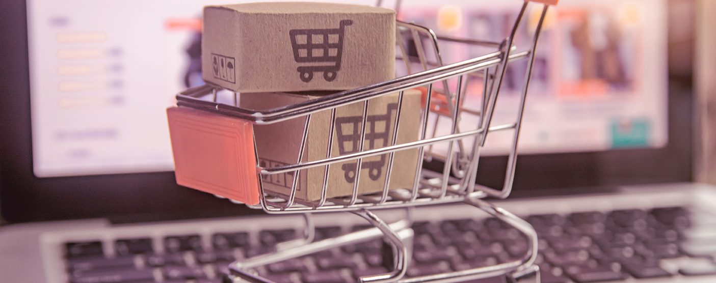 Small shopping cart with small shipping boxes inside it, sitting on top of a laptop.