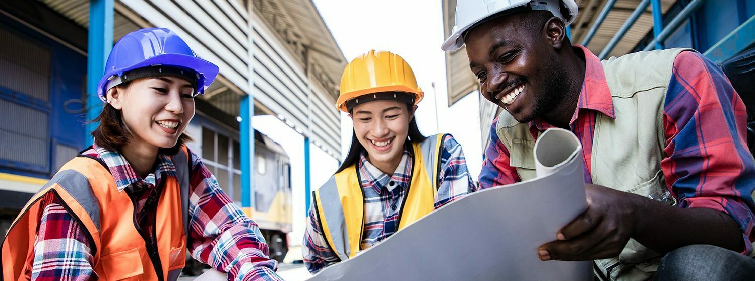 Three construction workers looking at a paper plan and smiling.