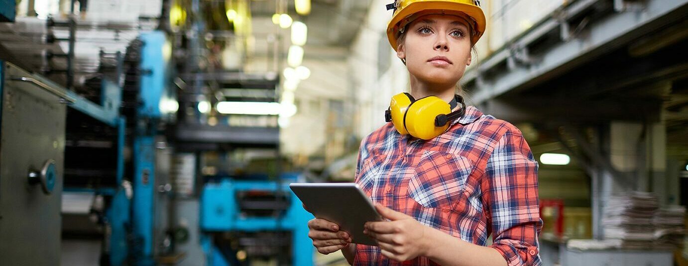 Woman in flannel shirt and yellow hard hat in a factory facility.