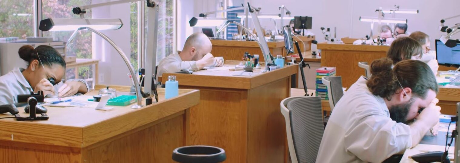 Quality assurance professionals inspect watches under magnifying glasses in laboratory.