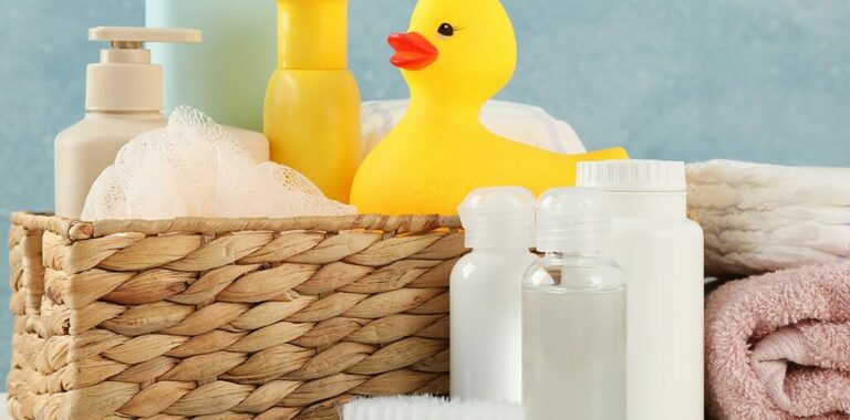 Baby bath accessories including a rubber duck, shampoo bottles, and a loofah in a wicker basket.