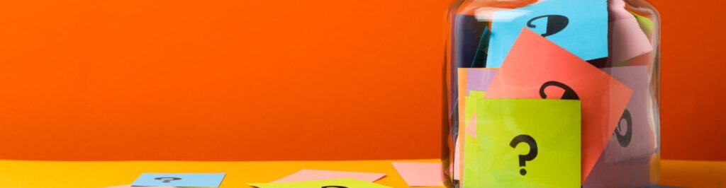 Colorful cards with question marks in glass jar on orange background.