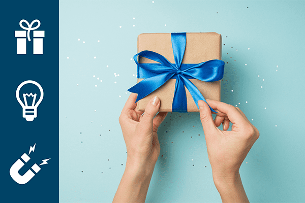 First person top view photo of hands unpacking craft paper giftbox with vivid blue satin ribbon bow over shiny sequins on isolated pastel blue background.