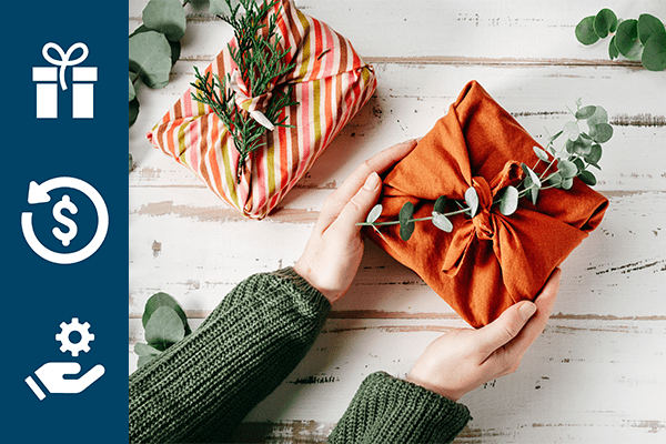 Orange wrapped gift with eucalyptus on top being held by woman wearing green sweater.