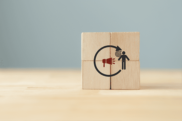 Four wooden blocks stacked together in a square with an icon of a megaphone, a target, and a person on the front.