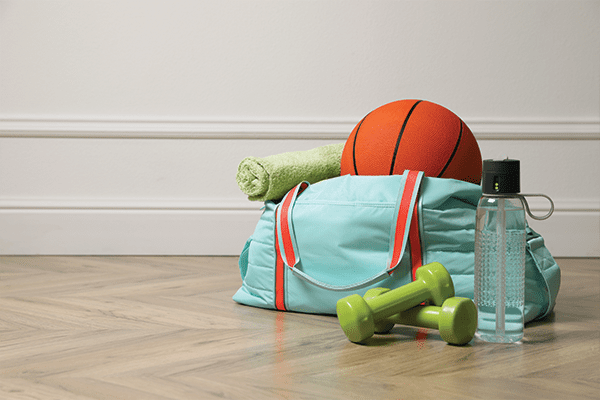 Brigt gym bag, basketball, weights, towel and water bottle sitting on wood floor.