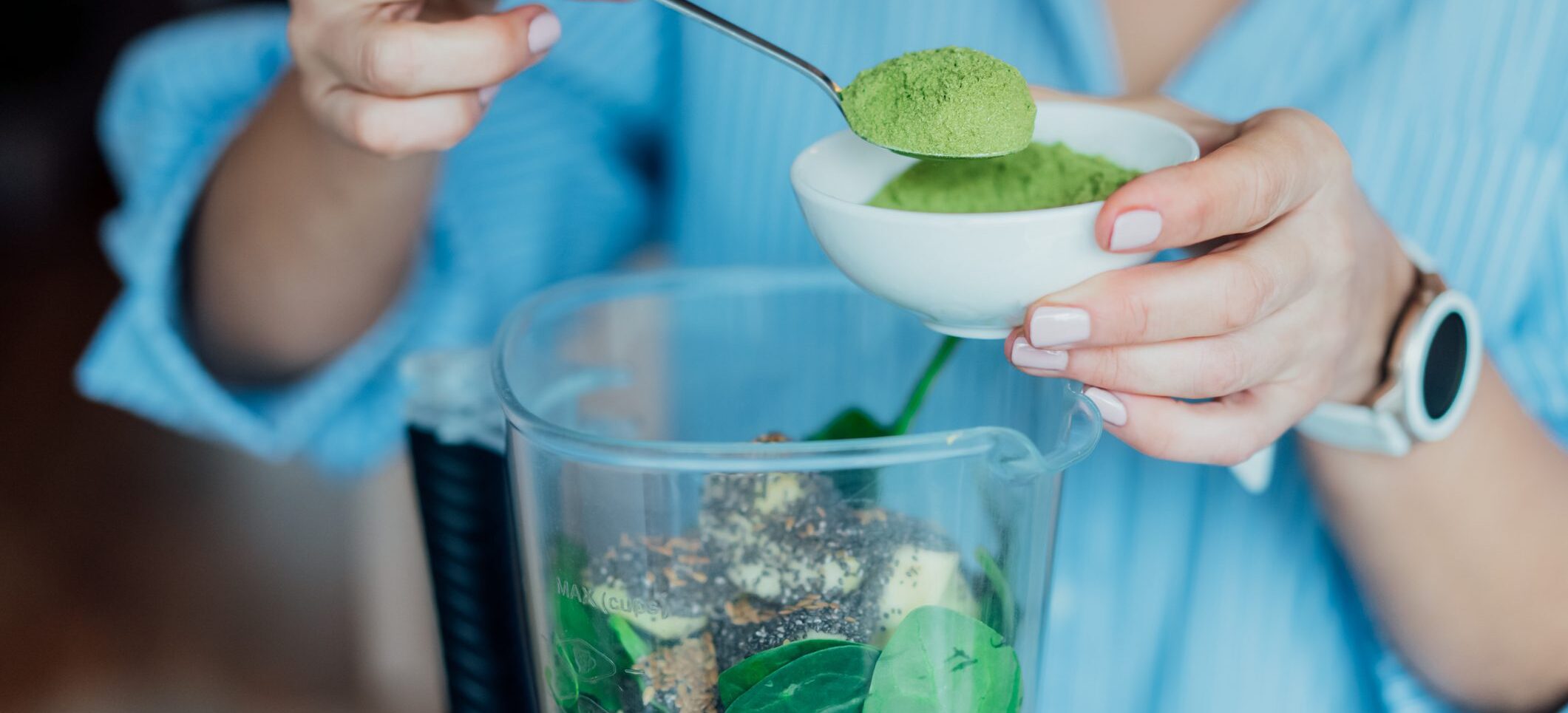 Close up woman adding wheat grass green powder during making smoothie on the kitchen. Superfood supplement. Healthy detox vegan diet. Healthy dieting eating, weight loss program. Selective focus.