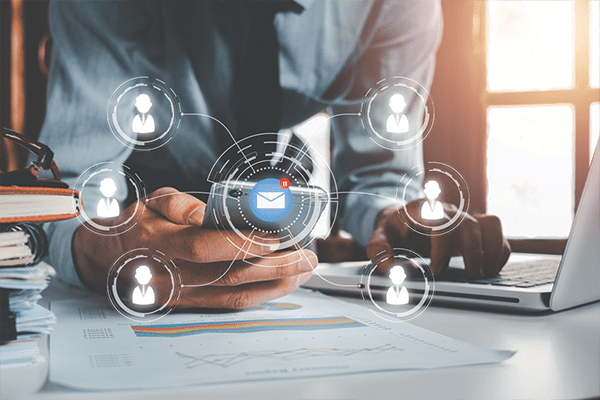 Man holding pone and using laptop with icons of people overlayed. Sunny window in the background.