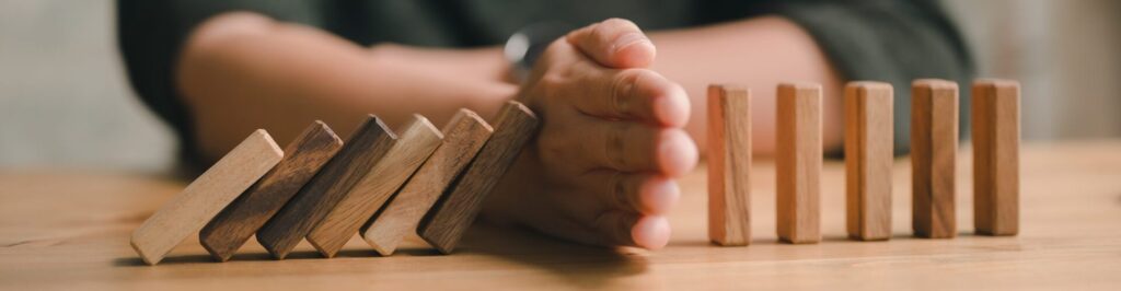 Woman putting her hands in front of a stack of falling wooden rectangles to stop them from continuing to fall.