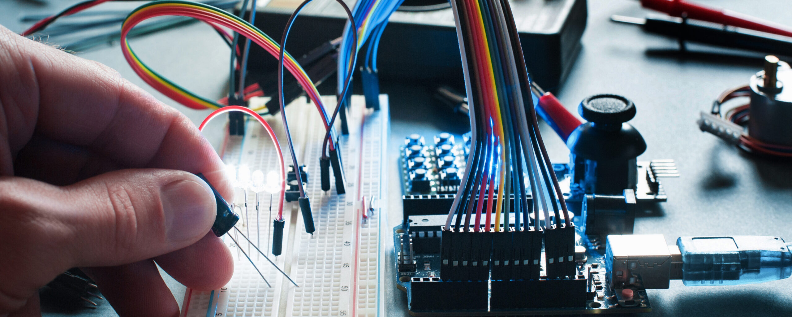 Circuits creation with electronic components. Closeup on programmer hand connecting led with breadboard and microcontroller. Programming, electronics development, innovation in technologies