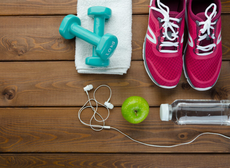 Fitness concept with sneakers dumbbells bottle of water and apple on wooden table background