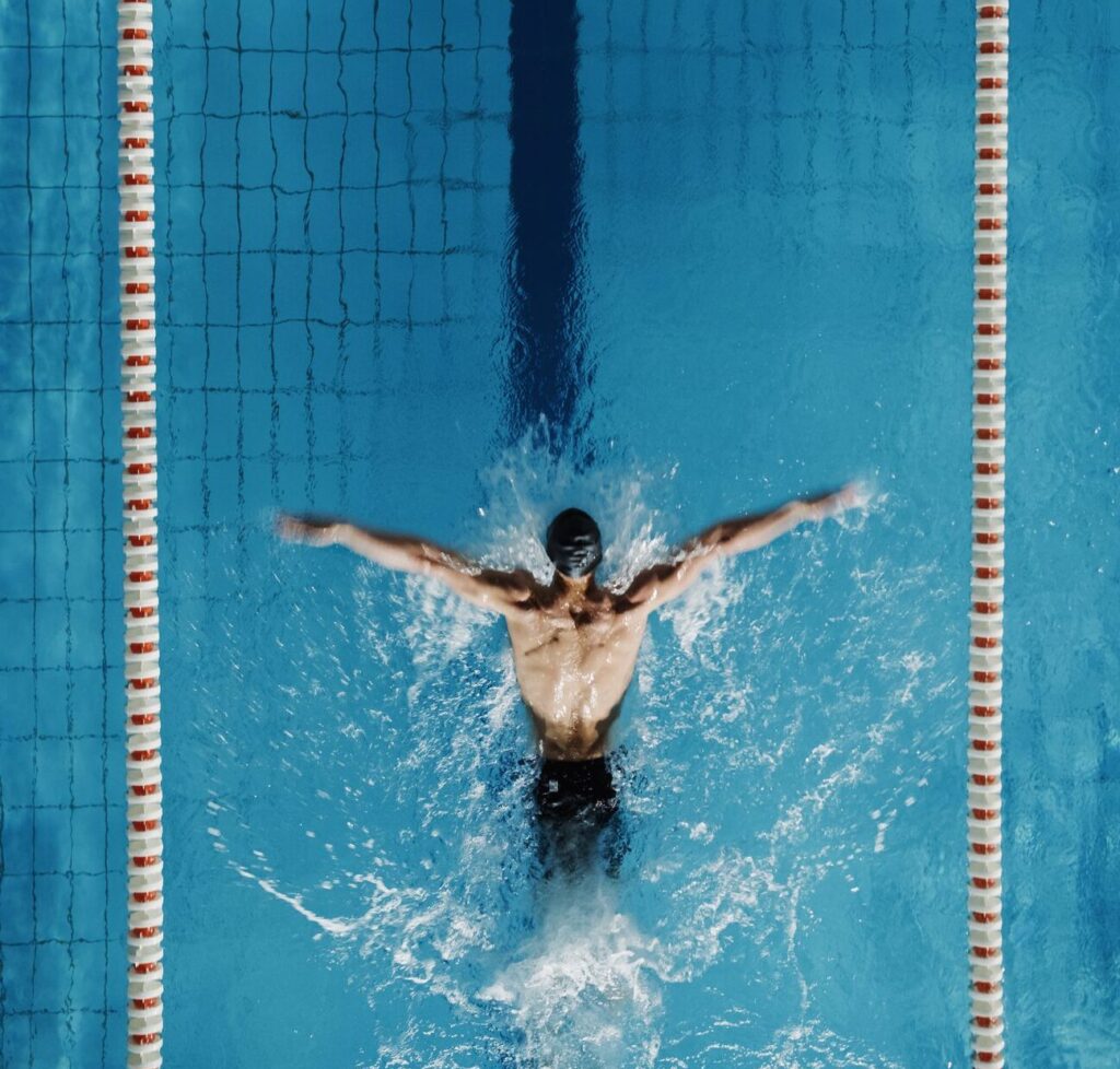 Aerial Top View Male Swimmer Swimming in Swimming Pool. Professional Determined Athlete Training for the Championship, using Butterfly Technique. Top View Shot