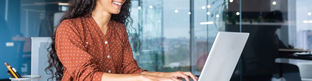 Woman in orange shirt typing on computer and smiling.