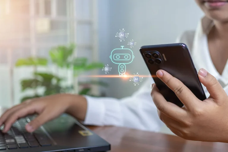 Woman typing on laptop and using phone with AI robot popping up.