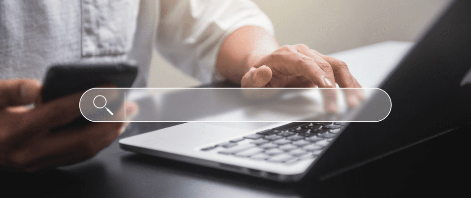 Hands holding phone and typing on laptop with search bar