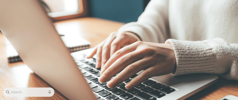 hands typing on laptop with search bar visible in corner