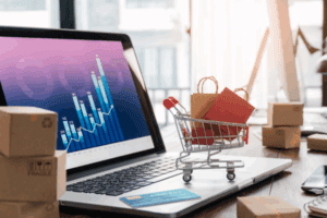 Shopping bags in shopping cart and credit card on laptop with paper boxes on table and sales data economic growth graph on screen, buying and selling services online on network, online shopping and e-commerce concept