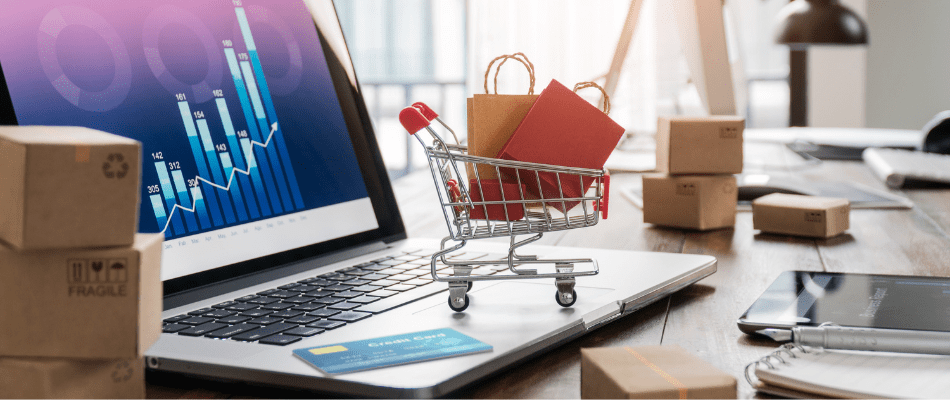 Shopping bags in shopping cart and credit card on laptop with paper boxes on table and sales data economic growth graph on screen, buying and selling services online on network, online shopping and e-commerce concept