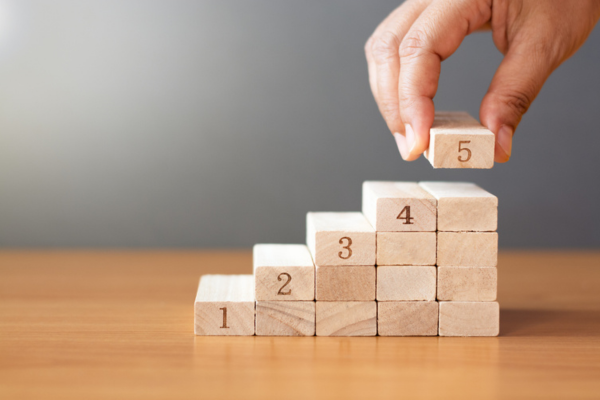 Women hand putting a wooden block on top and arranging wooden blocks stacking on wooden table in the shape of a staircase, Business concept for growth success process.