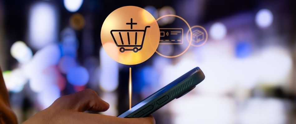 Image of a hand holding a mobile phone with shopping icons projected from the phone