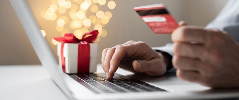 Photo of a laptop, wrapped gift, and hands typing while holding a credit card