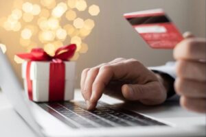 Photo of a laptop, wrapped gift, and hands typing while holding a credit card