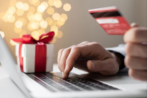 Photo of a laptop, wrapped gift, and hands typing while holding a credit card