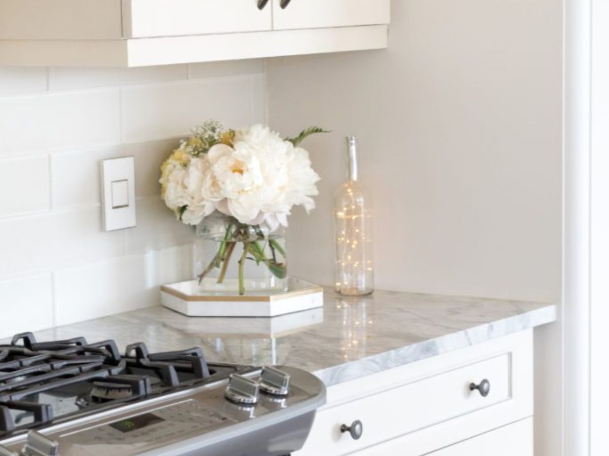 Bright white kitchen with a light switch on the tile backsplash above a marble counter and gas range