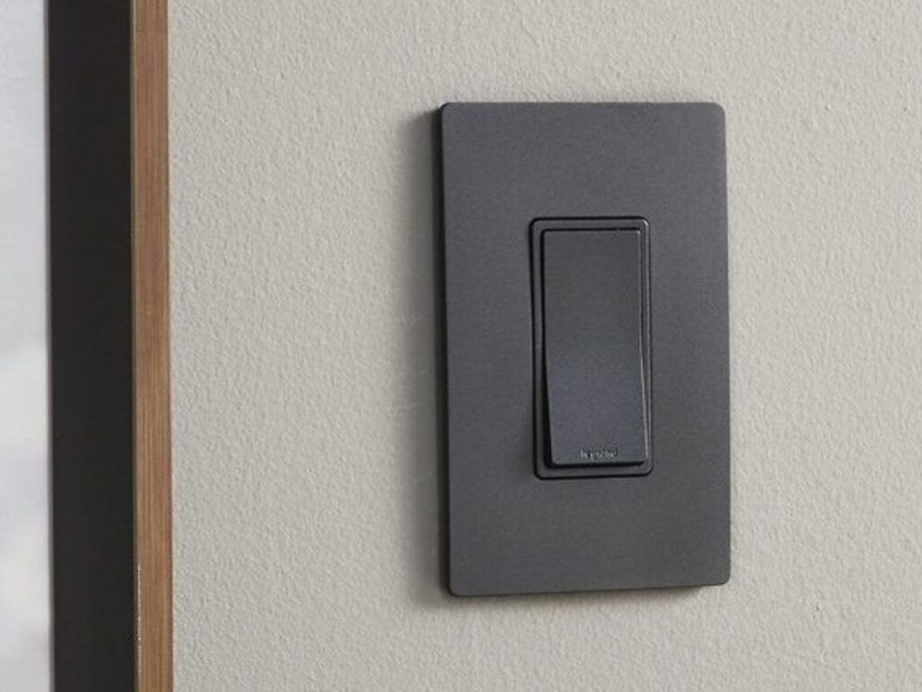 Dark gray rocker light switch with a matching wall plate on a textured off-white wall