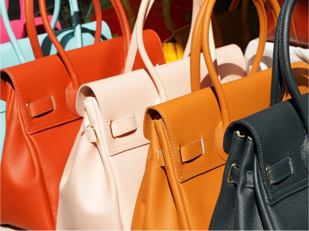 Orange, blush, tan and navy leather handbags lined up side by side
