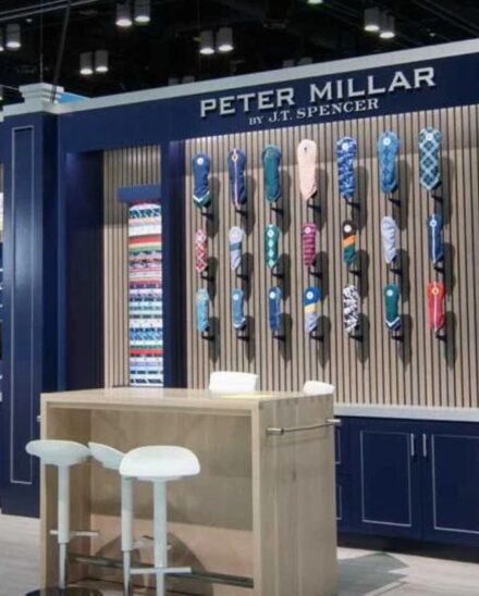 Peter Millar golf trade show booth with a wall of headcovers, branded golf bags and a high-top table with stools
