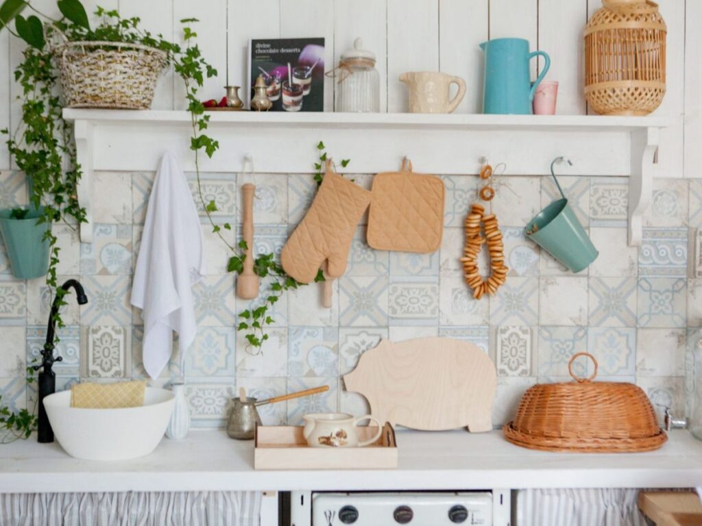 Patterned tile backsplash under a white shelf, with hanging oven mitts, a towel and woven basket