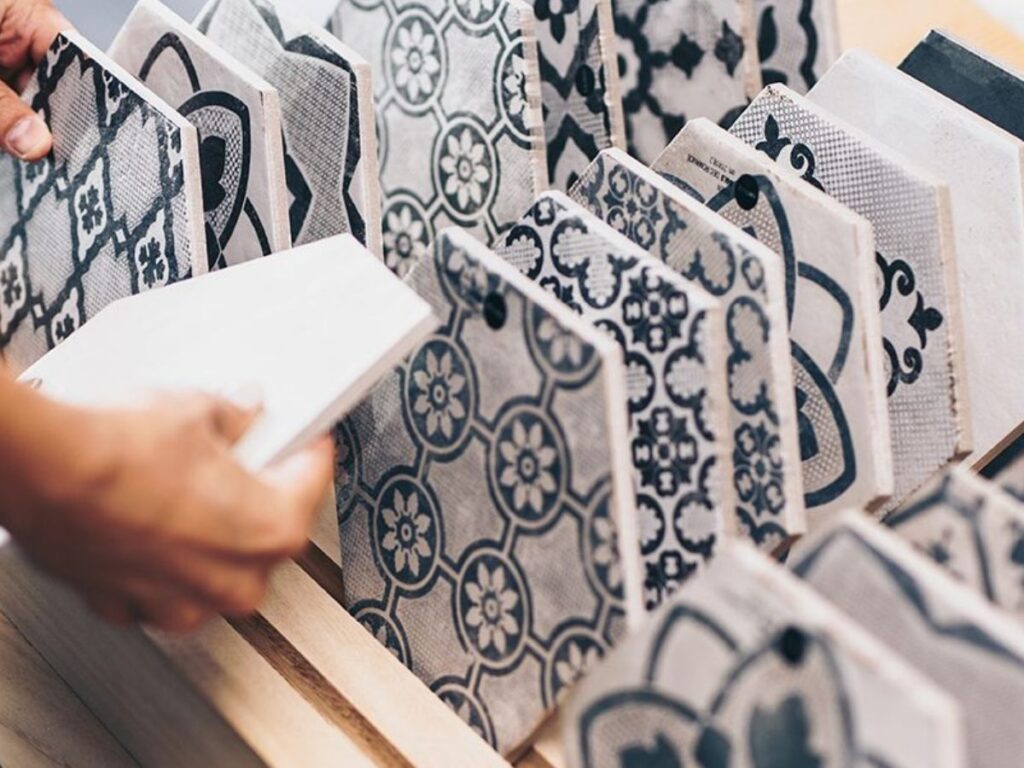 Hand flipping through a rack of patterned gray and white ceramic tile samples